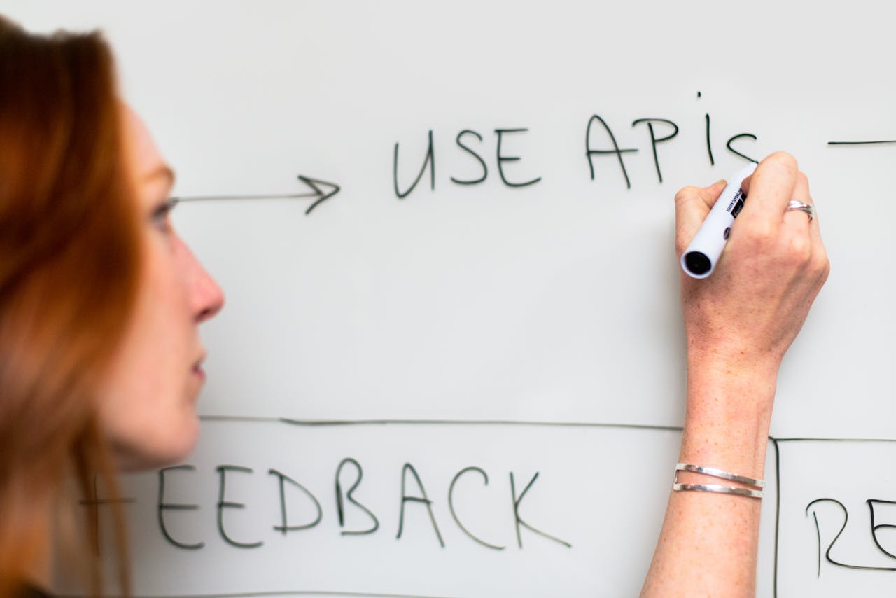 our-story A woman writes 'Use APIs' on a whiteboard, focusing on software planning and strategy.